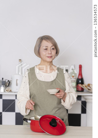 Senior woman tasting the food she cooked in the kitchen Senior woman tasting the food she cooked in the kitchen 136534573