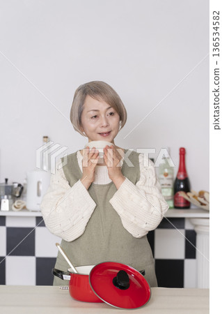 Senior woman tasting the food she cooked in the kitchen Senior woman tasting the food she cooked in the kitchen 136534582