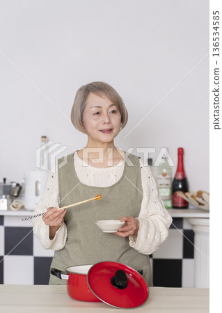 Senior woman tasting the food she cooked in the kitchen Senior woman tasting the food she cooked in the kitchen 136534585