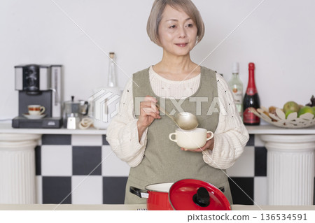 Senior woman tasting the food she cooked in the kitchen Senior woman tasting the food she cooked in the kitchen 136534591