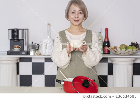 一位老婦人在廚房品嚐自己做的餐點。 一位老婦人在廚房品嚐自己做的餐點。 136534593