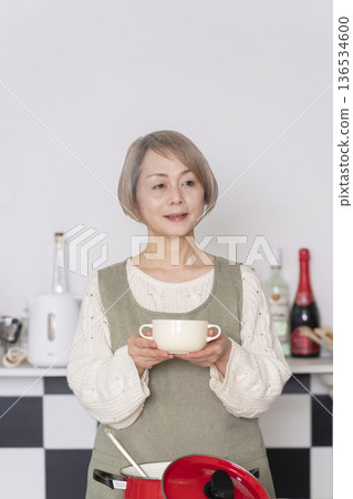 Senior woman tasting the food she cooked in the kitchen Senior woman tasting the food she cooked in the kitchen 136534600