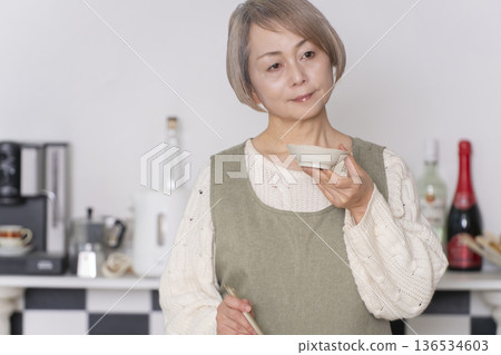 一位老婦人在廚房品嚐自己做的餐點。 一位老婦人在廚房品嚐自己做的餐點。 136534603