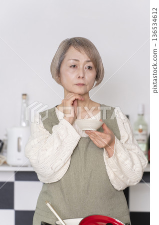 一位老婦人在廚房品嚐自己做的餐點。 一位老婦人在廚房品嚐自己做的餐點。 136534612