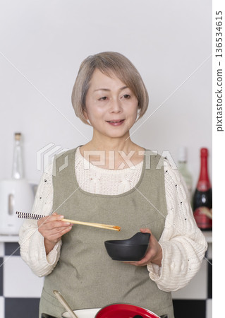 Senior woman tasting the food she cooked in the kitchen Senior woman tasting the food she cooked in the kitchen 136534615