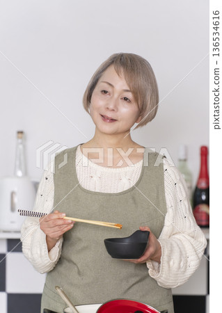 一位老婦人在廚房品嚐自己做的餐點。 一位老婦人在廚房品嚐自己做的餐點。 136534616