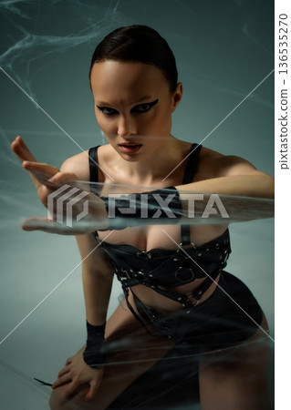 Intense portrait of a woman in black leather attire reaching through cobwebs Intense portrait of a woman in black leather attire reaching through cobwebs 136535270