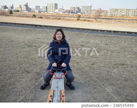 A middle-aged woman playing on a seesaw in a park on a winter afternoon 136535430
