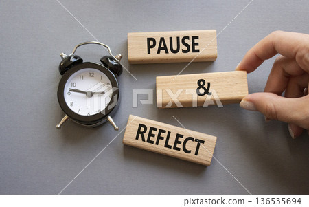 Pause and Reflect symbol. Concept words Pause and Reflect on wooden blocks. Businessman hand. Beautiful grey background with alarm clock. Business and Pause and Reflect concept. Copy space. 136535694