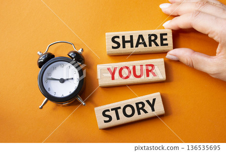 Share your story symbol. Wooden blocks with words Share your story. Businessman hand. Beautiful orange background with alarm clock. Business and Share your story concept. Copy space. 136535695