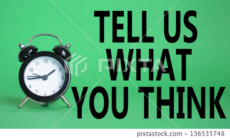 Tell us what you think symbol. Wooden blocks with words Tell us what you think. Beautiful green background with alarm clock. Business and Tell us what you think concept. Copy space. 136535748