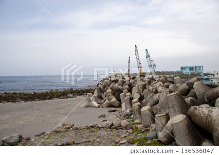 大量防浪塊沿著海岸線排列，旁邊還有一台港口起重機。 136536047