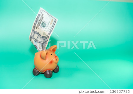 A piggy bank with a twenty-dollar bill sticking out, set against a vivid teal background, illustrating savings. A piggy bank with a twenty-dollar bill sticking out, set against a vivid teal background, illustrating savings. 136537725