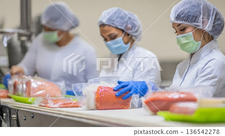 Food industry workers in hygienic uniforms, masks, and gloves carefully prepare and package fresh salmon fillets on a conveyor belt, highlighting seafood production safety standards. AI Generated Food industry workers in hygienic uniforms, masks, and gloves carefully prepare and package fresh salmon fillets on a conveyor belt, highlighting seafood production safety standards. AI Generated 136542278