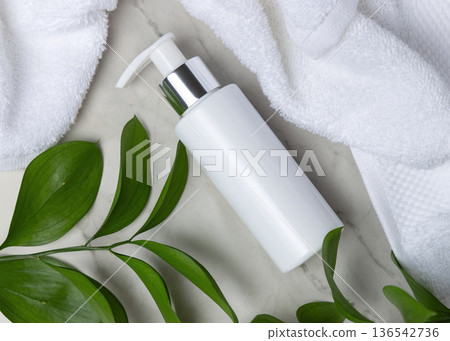 Mockup of blank white pump bottle near white bath terry towel and green leaves. Unbranded cosmetic 136542736