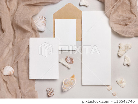 Cards and envelopes on beige stone with seashells top view, mockup. Coastal wedding stationery set 136542740