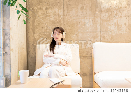 一位女士坐在咖啡館的沙發上,戴著耳機聽音樂。 一位女士坐在咖啡館的沙發上,戴著耳機聽音樂。 136543188