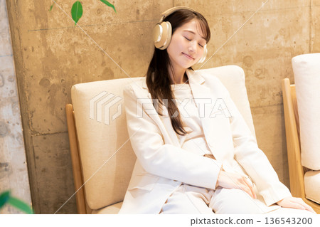 一位女士坐在咖啡館的沙發上,戴著耳機聽音樂。 一位女士坐在咖啡館的沙發上,戴著耳機聽音樂。 136543200