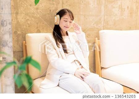 A woman sitting on a sofa in a cafe and listening to music with headphones 136543203