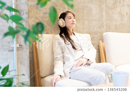 A woman sitting on a sofa in a cafe and listening to music with headphones 136543206