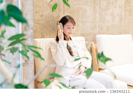 一位女士坐在咖啡館的沙發上，戴著耳機聽音樂。 136543211