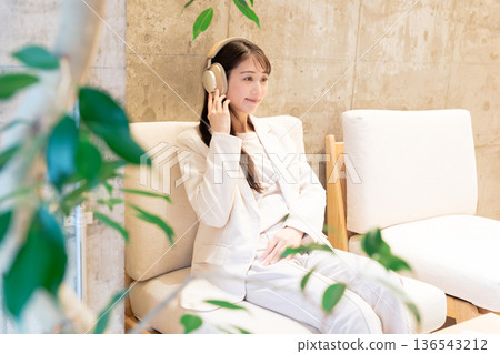 A woman sitting on a sofa in a cafe and listening to music with headphones A woman sitting on a sofa in a cafe and listening to music with headphones 136543212