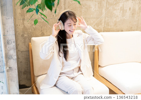 一位女士坐在咖啡館的沙發上,戴著耳機聽音樂。 一位女士坐在咖啡館的沙發上,戴著耳機聽音樂。 136543218
