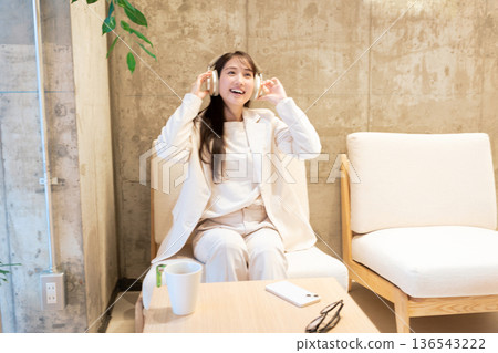 一位女士坐在咖啡館的沙發上,戴著耳機聽音樂。 一位女士坐在咖啡館的沙發上,戴著耳機聽音樂。 136543222