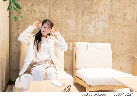 一位女士坐在咖啡館的沙發上,戴著耳機聽音樂。 一位女士坐在咖啡館的沙發上,戴著耳機聽音樂。 136543224