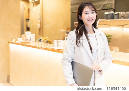 年輕女子站在咖啡館裡，手裡拿著筆記型電腦。 136543400