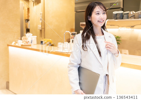 Young woman standing with a laptop in a cafe 136543411