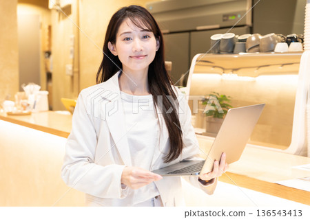 Young woman standing with a laptop in a cafe Young woman standing with a laptop in a cafe 136543413