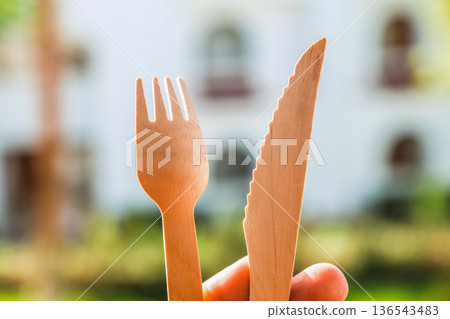 A pair of wooden cutlery fork and knife in hand on bokeh nature background 136543483