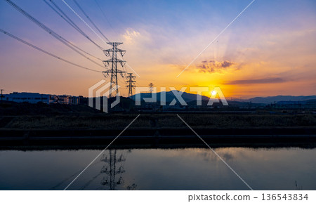 A view of the setting sun and steel towers reflected on the surface of the Homan River 136543834