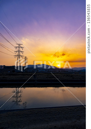 A view of the setting sun and steel towers reflected on the surface of the Homan River 136543835