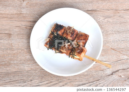 grilled white tofu wrapped pork bacon stabbing in wooden stick topping dry seaweed and fish dressing soy sauce on plate 136544297