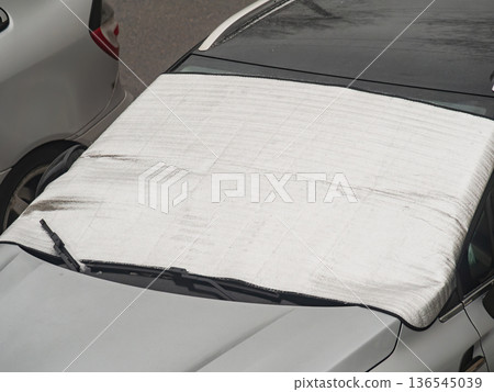 A car is parked on a snowy street with a tarpaulin covering its windshield. A car is parked on a snowy street with a tarpaulin covering its windshield. 136545039