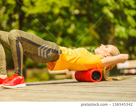 Girl doing exercises outdoor, using roller 136545342
