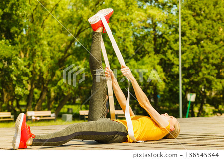 Girl doing exercises outdoor, using fit band. Girl doing exercises outdoor, using fit band. 136545344
