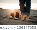 Barefoot on Sandy Beach at Sunrise with Shoes Nearby 136547058