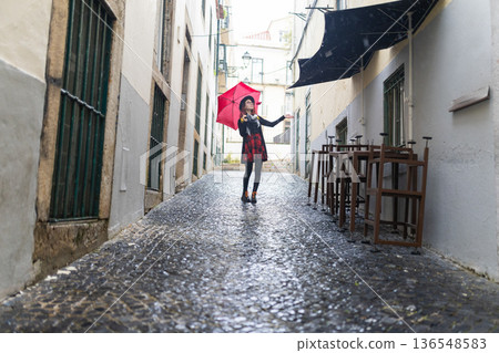 Woman holding red umbrella exploring wet european street Woman holding red umbrella exploring wet european street 136548583