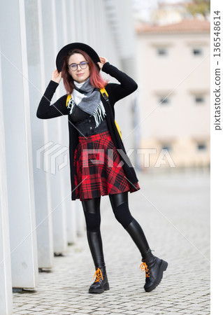 Young woman posing outdoors wearing fashionable plaid skirt 136548614