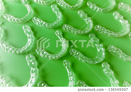 Transparent dental aligners arranged on a green background, showcasing their unique shape and design for orthodontic treatment and teeth straightening solutions 136549307