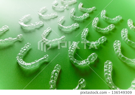 Clear orthodontic aligners arranged on a green background, showcasing multiple shapes and sizes for dental correction and alignment purposes 136549309