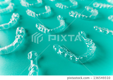Clear dental aligners arranged on a turquoise background, showcasing various sizes and shapes for orthodontic treatment and teeth straightening solutions 136549310