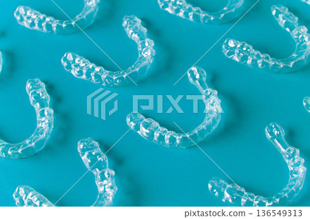Clear orthodontic aligners arranged on a turquoise background, showcasing their transparent design and unique shape for teeth straightening solutions 136549313