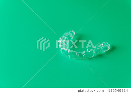 Clear dental aligner placed on a vibrant green background, showcasing its transparent design and unique shape for orthodontic treatment and teeth straightening Clear dental aligner placed on a vibrant green background, showcasing its transparent design and unique shape for orthodontic treatment and teeth straightening 136549314