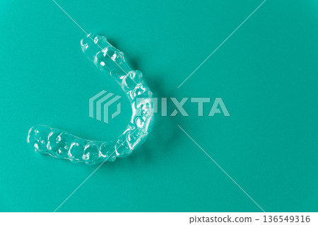 Clear dental aligner placed on a solid turquoise background, showcasing its transparent design and unique shape for orthodontic treatment and teeth straightening Clear dental aligner placed on a solid turquoise background, showcasing its transparent design and unique shape for orthodontic treatment and teeth straightening 136549316
