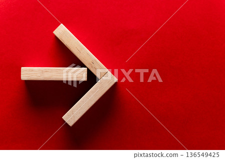 Wooden blocks arranged in an arrow shape on a vibrant red background, showcasing geometric design and minimalistic style for creative concepts from left to right Wooden blocks arranged in an arrow shape on a vibrant red background, showcasing geometric design and minimalistic style for creative concepts from left to right 136549425