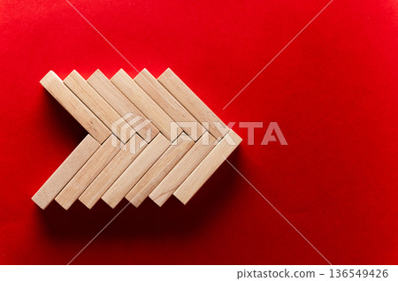 Wooden blocks arranged in an arrow shape on a vibrant red background, showcasing geometric design and creative construction with a minimalist aesthetic Wooden blocks arranged in an arrow shape on a vibrant red background, showcasing geometric design and creative construction with a minimalist aesthetic 136549426